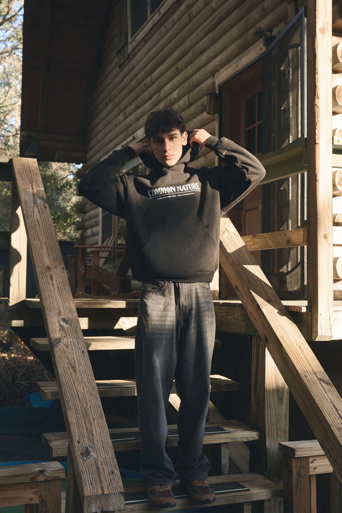 Man in a black Common Nature hoodie pulling up his hood on cabin steps