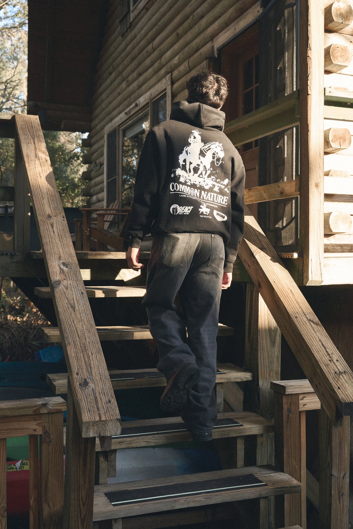 Man walking up cabin steps in a black Common Nature hoodie, back graphic visible