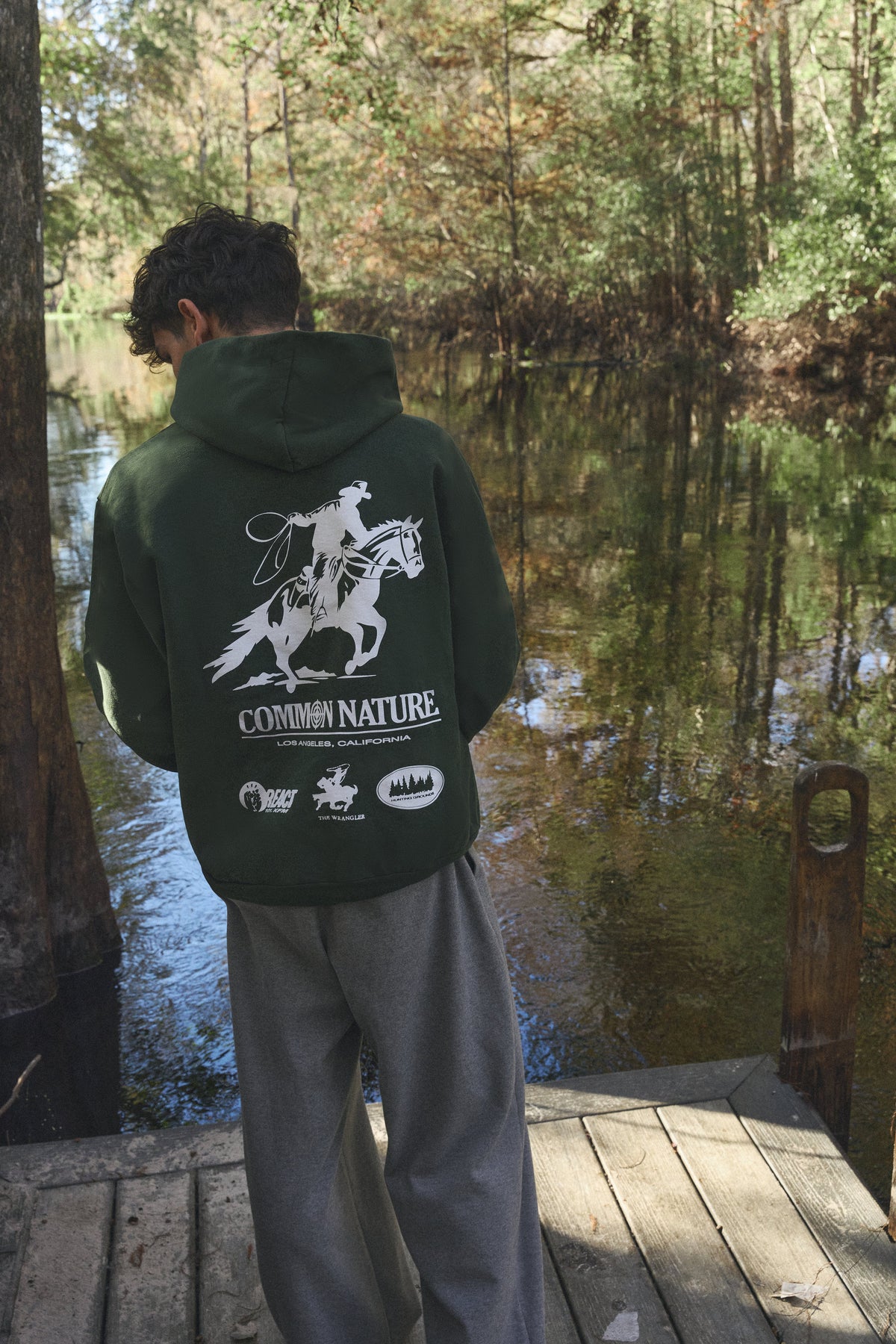Back graphic of a forest green Common Nature hoodie by the water
