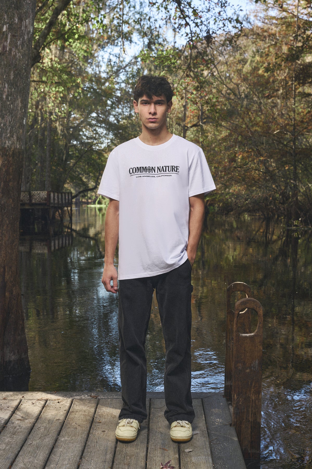 Man in a white Common Nature tee and black jeans on a dock