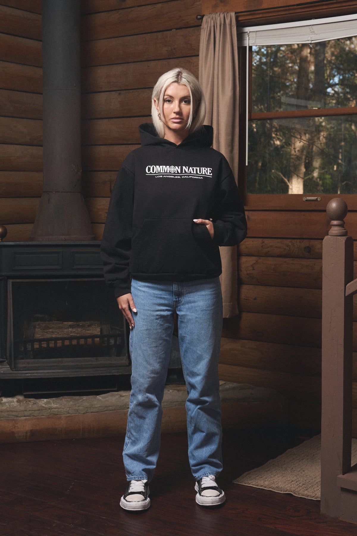 Woman in a black Common Nature hoodie and jeans inside the cabin