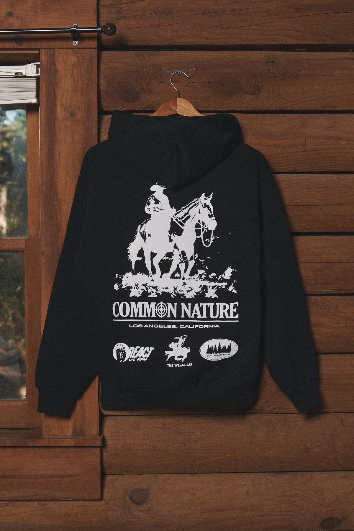 Black Common Nature graphic hoodie hanging on a cabin wall
