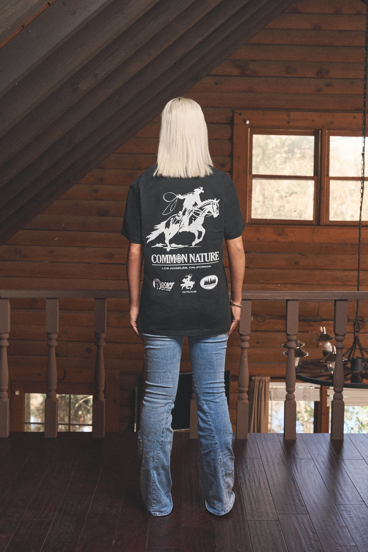 Back graphic of a black Common Nature tee on a woman in a cabin loft