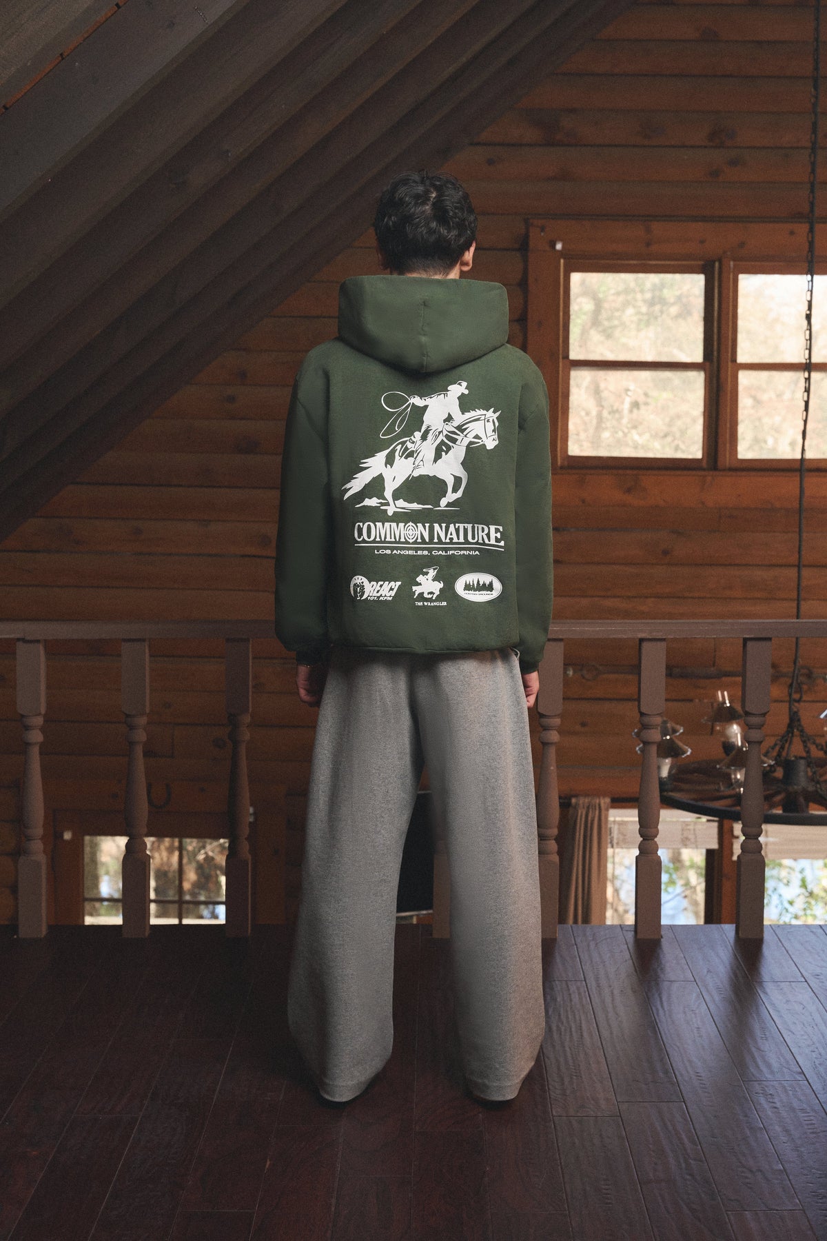 Back graphic of a forest green Common Nature hoodie in a cabin loft