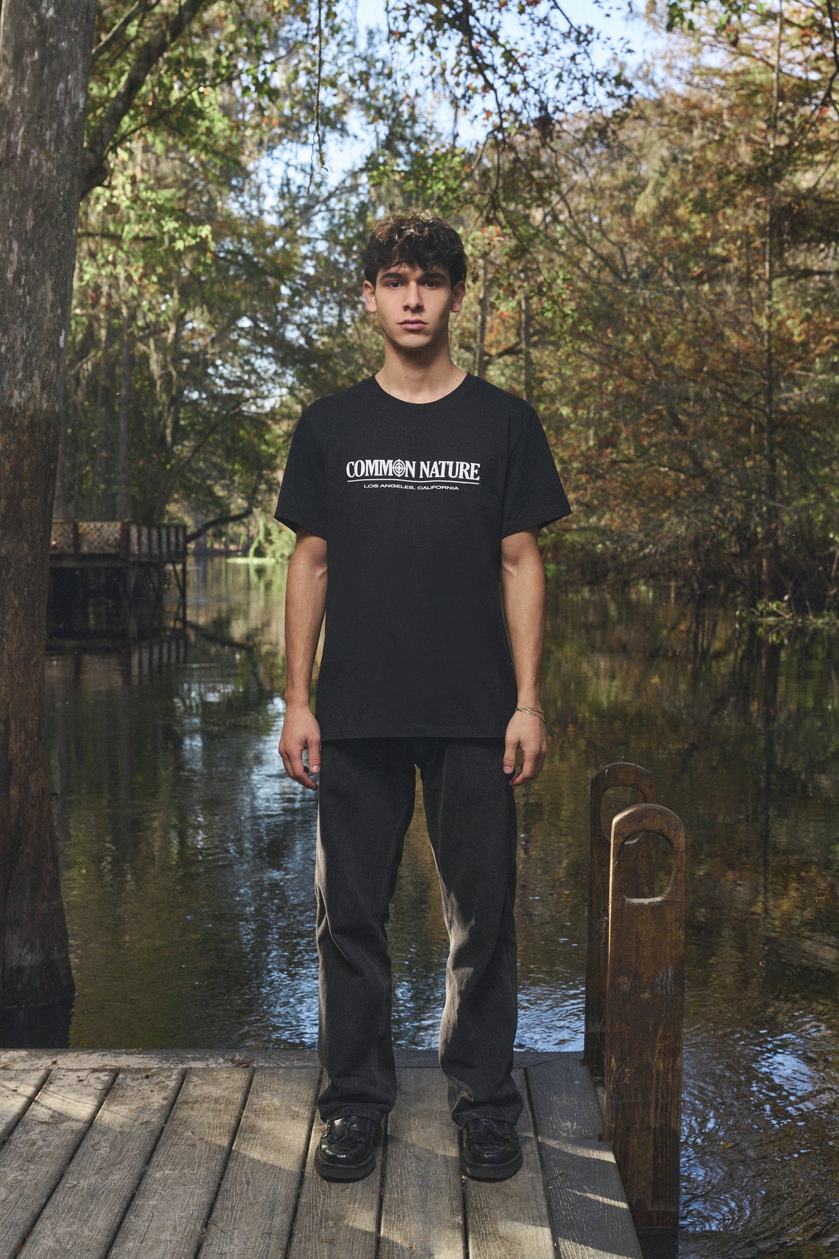 Man in a black Common Nature tee on a dock by the water