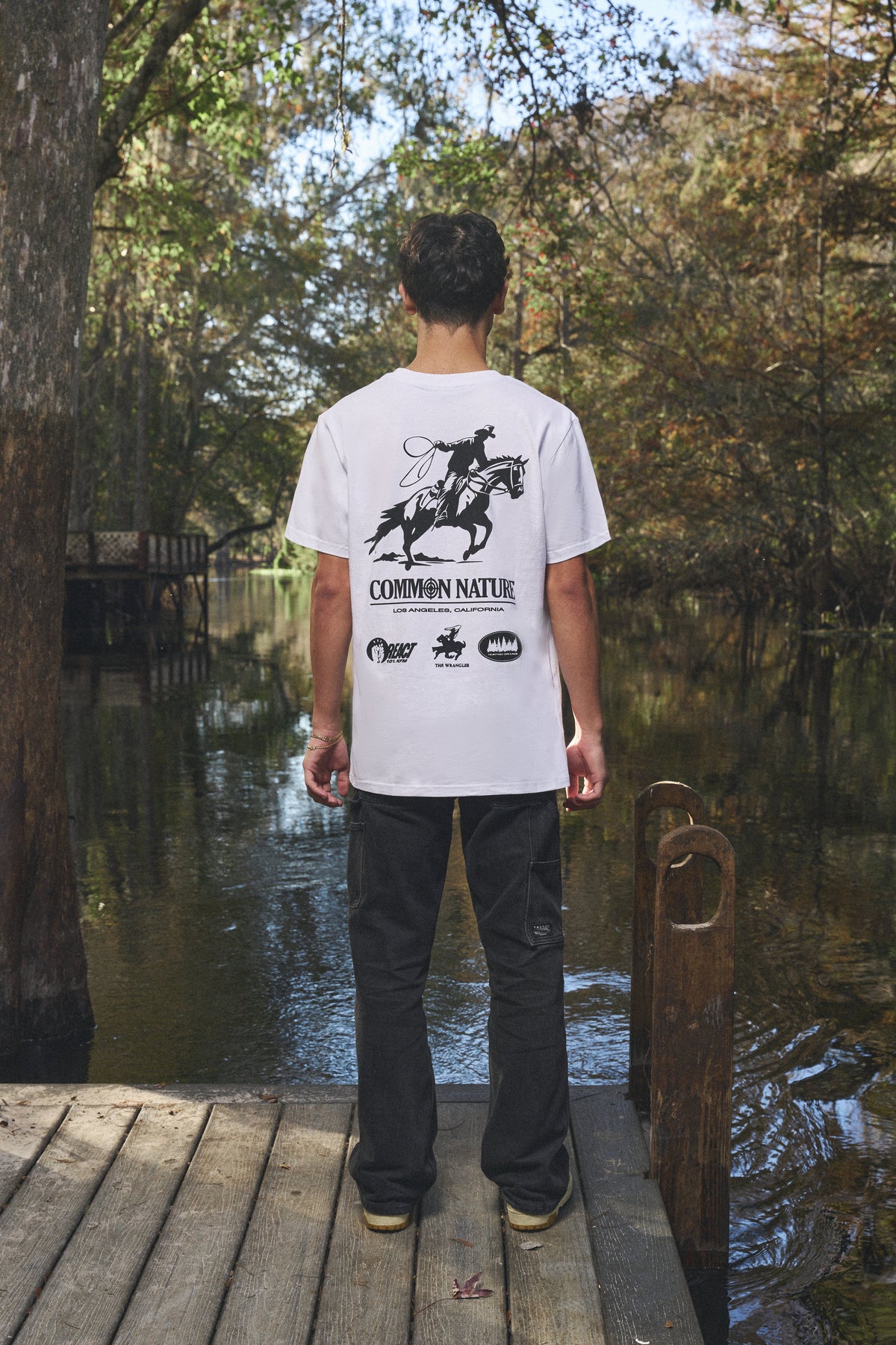 Back graphic of a white Common Nature tee on a dock by the water