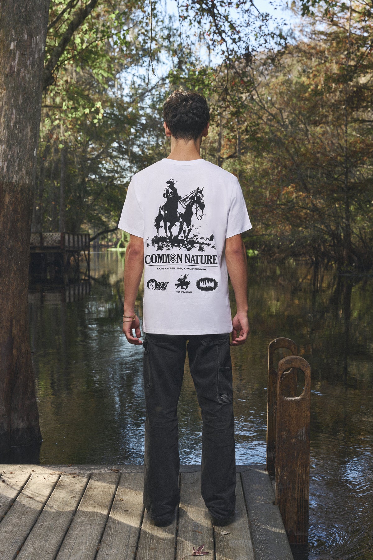 Back graphic of a white Common Nature tee by the water
